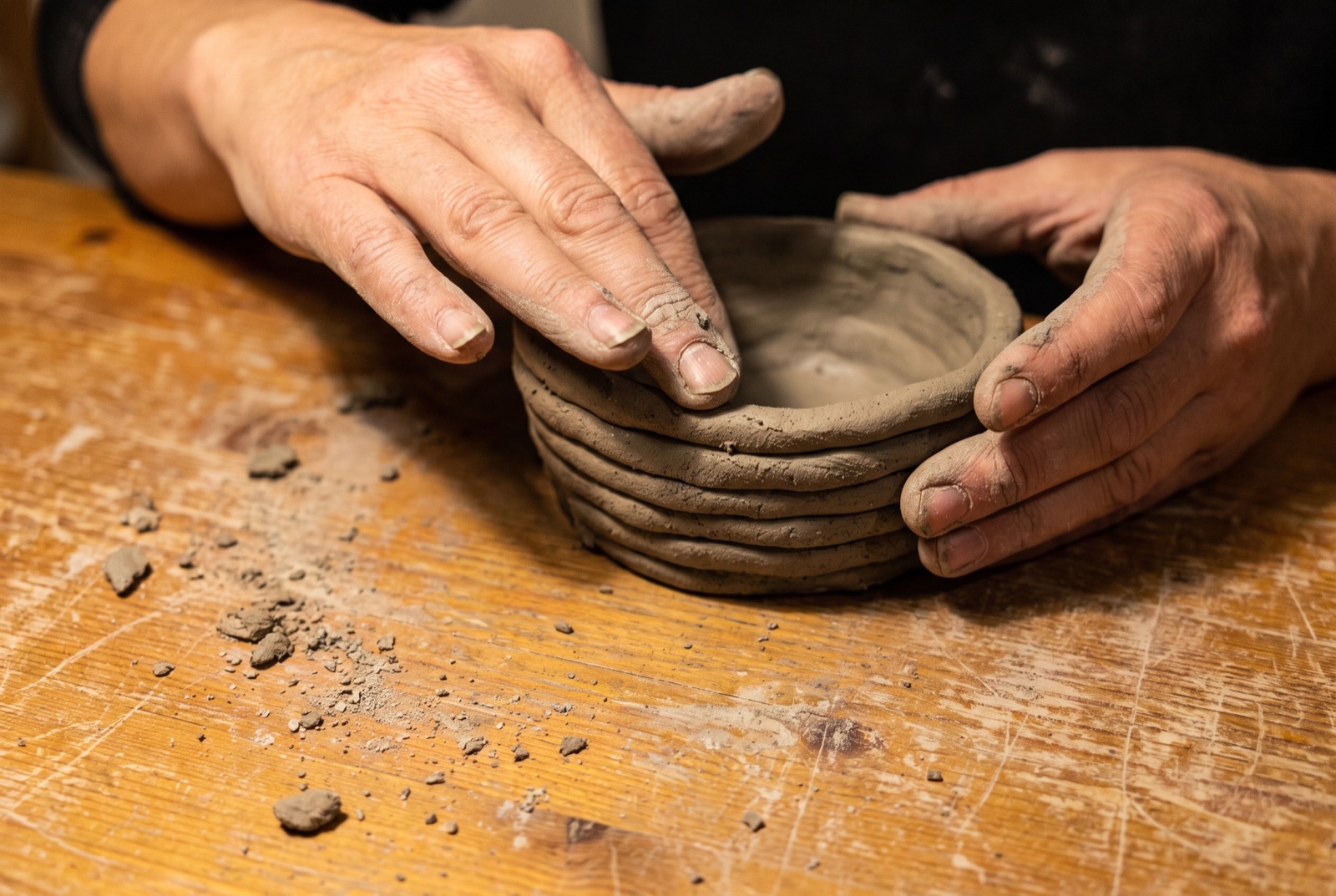 Mains d'adulte montant un bol à la technique du colombin lors d'un atelier de modelage